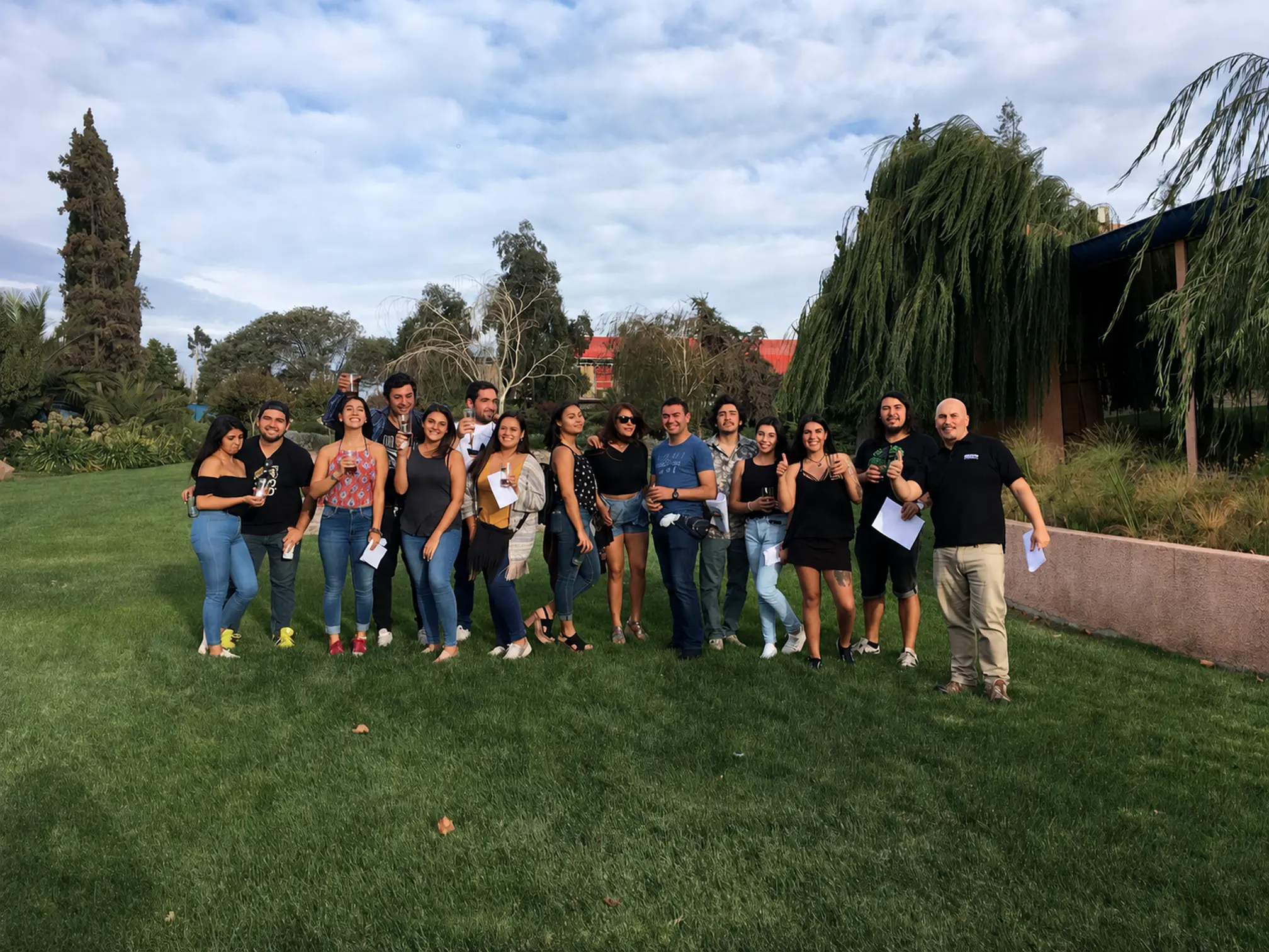 Grupo de visitantes posando al aire libre en el jardín, cada uno con su bebida