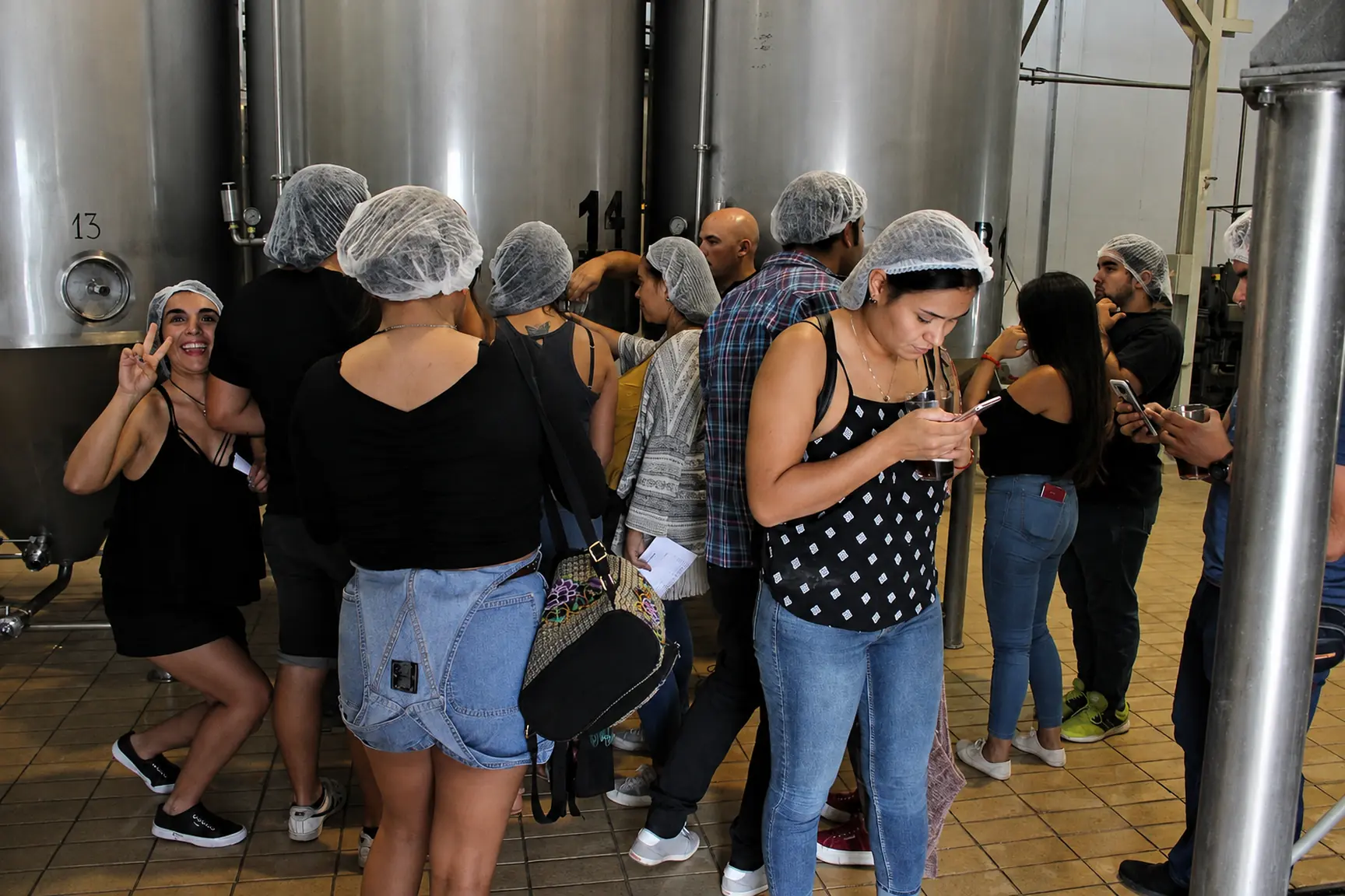 Grupo de visitantes con cofia junto a los tanques de fermentación de acero inoxidable