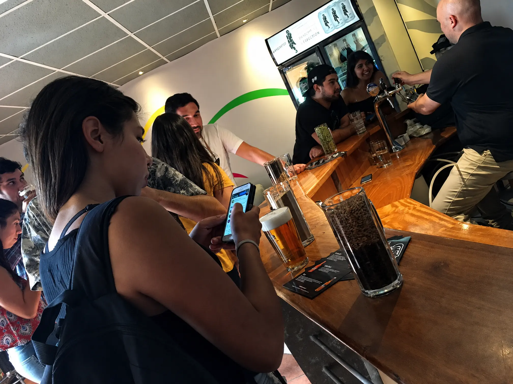 Barman sirviendo cerveza desde el grifo en la barra, con jarras y granos sobre la mesa